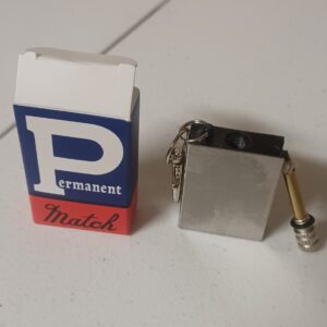 A permanent match alongside its packaging, featuring a small metallic lighter and a matchbox design. A permanent match alongside its packaging, featuring a small metallic lighter and a matchbox design.